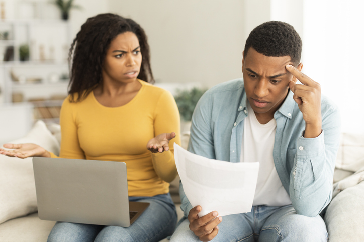Angry unhappy millennial african american lady quarreling at guy over debts and bills with laptop